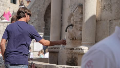 Hombre-Caucásico-Adulto-Joven-Llenando-Una-Botella-De-Agua-En-La-Histórica-Ciudad-De-Dubrovnik