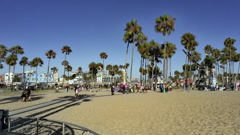 People-walking-on-sand-at-the-Venice-beach-Boardwalk,-during-golden-hour,-in-Los-Angeles,-California,-USA---Handheld-shot