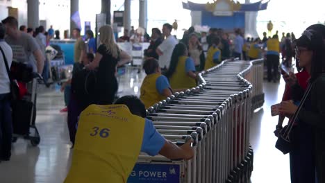 Los-Trabajadores-Del-Aeropuerto-Recogen-Los-Carros-Con-La-Multitud-De-Personas-Al-Fondo.