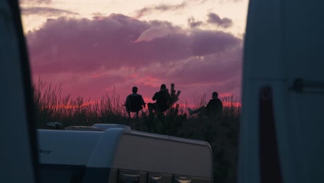 Silhouette-People-chilling-on-top-of-a-dune,-at-the-trailer-park,-dusk-in-Kalajoki,-Finland