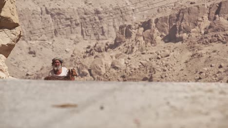 Omani-Goat-farmer-man-carrying-lost-goat-through-the-harsh-Desert-heat---Wide-Tracking-shot