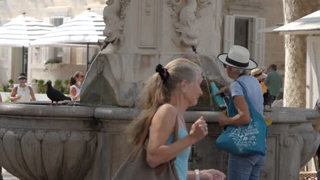 Una-Paloma-Se-Va-Volando-Mientras-Una-Mujer-Viene-A-Llenar-Agua-De-Una-Fuente-Histórica-En-Dubrovnik.