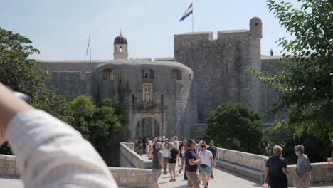 Fotógrafa-Tomando-Fotos-Del-Castillo-De-Dubrovnik-Con-Bandera-Ondeando,-Vista-En-Movimiento