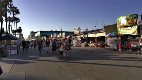 Masked-people-walking-between-shops-at-the-Venice-Boardwalk,-during-golden-hour,-in-Los-Angeles,-California,-USA---Quiet-do-to-the-Coronavirus-pandemic