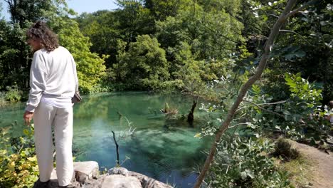 Beautiful-woman-with-curly-hair-enjoys-view-of-Plitvice-lakes,-dolly-backward-view