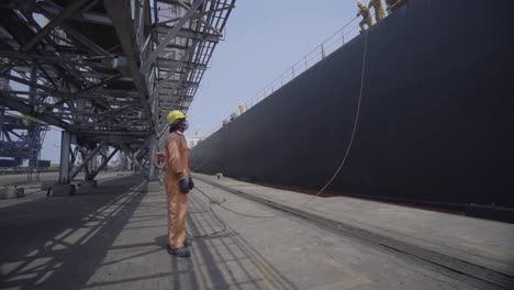 Trabajador-Portuario-Con-Casco-Y-Máscara-Sosteniendo-Cuerda-De-Amarre-De-Un-Gran-Barco-En-El-Puerto