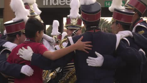 Banda-De-Música-Reunida-Y-Preparándose-Para-Actuar-En-El-Desfile-Del-Día-De-Los-Caídos:-Plano-De-Seguimiento-Medio-Largo