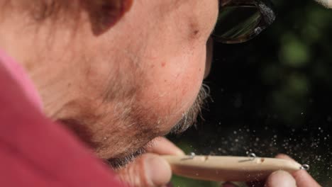 Old-man-blow-dust-after-drill-wooden-piece,-slow-motion-close-up