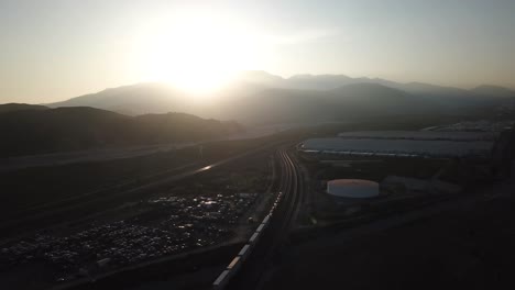 Vista-Aérea-De-La-Puesta-De-Sol-Sobre-El-Valle-De-Sand-Bernardino-Y-El-Tren-De-Carga-BNSF-En-El-Ferrocarril,-California,-EE.UU.