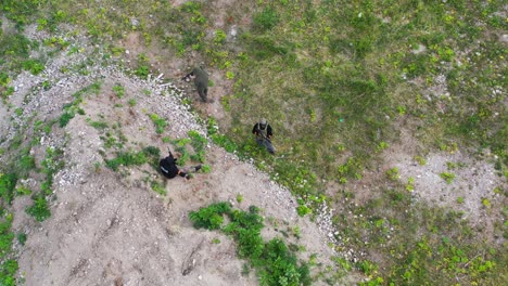 Flying-over-airsoft-players-take-cover-behind-gravel-stack,-war-game-in-action