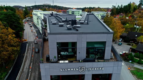 Aerial-drone-backward-moving-shot-over-a-black-high-rise-office-modern-building-along-the-intersection-of-a-road-Stockholm,-Sweden-at-daytime