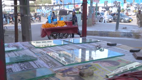 Backward-slow-motion-shot-of-a-roadside-stall-of-a-man-selling-newspaper-during-a-sunny-afternoon-at-Saddar-Bazar-Street-of-Karachi-in-Pakistan