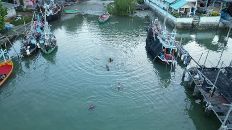 Children-seen-from-above-swimming-at-an-estuarine-fishing-village-as-the-drone-move-forward,-Bang-Pu-Fishing-Village,-Sam-Roi-Yot-National-Park,-Prachuap-Khiri-Khan,-Thailand