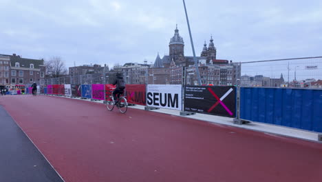 Cyclist-crossing-a-colorful-bridge-with-urban-museum-banners-in-Amsterdam