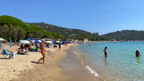 Gente-Disfrutando-De-Un-Divertido-Día-Soleado-De-Playa-De-Verano-En-Cavalière-Lavandou-Al-Sur-De-Francia,-Hermosas-Aguas-Turquesas-Transparentes,-Vacaciones-Junto-Al-Mar,-Toma-De-4k