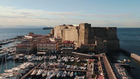 Drone-rising-near-a-fort-located-on-a-sea-coast-in-Italy,-Naples