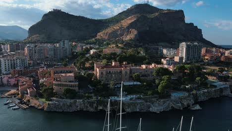 Drones-Volando-Hacia-Atrás-En-El-área-De-La-Bahía-De-Palermo,-Mientras-Que-Los-Hoteles,-Los-Veleros-Y-El-Mar-Azul-Son-Visibles-En-Primer-Plano-Y-La-Montaña-Monte-Pellegrino-Al-Fondo