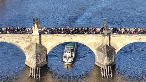 Barco-Turístico-Flota-Lentamente-En-El-Río-Bajo-El-Puente-De-Carlos-Lleno-De-Gente.