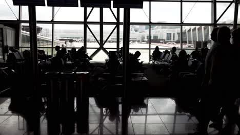 Vista-Cinematográfica-De-Viajeros-En-Silueta-Esperando-Y-Caminando-Dentro-Del-Salón-Del-Aeropuerto-Durante-El-Día.