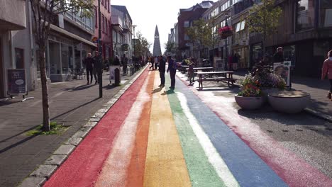 Calle-En-Reykjavik-Pintada-Con-Los-Colores-Del-Arco-Iris-Con-La-Iglesia-Luterana-Hallgrimskirkja-Al-Fondo-En-Islandia---Plano-Amplio