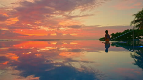 Chica-Con-Traje-De-Baño-Entrando-A-La-Piscina-Vacía-A-La-Orilla-Del-Mar-Disfrutando-De-Una-Hermosa-Puesta-De-Sol-Tropical