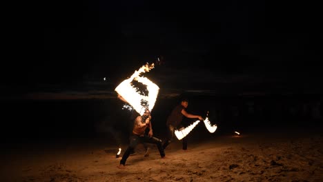 Bailarines-De-Fuego-Realizan-Un-Espectáculo-Nocturno-En-Una-Playa-De-Arena-En-Krabi,-Tailandia,-Con-Llamas-Dinámicas-Sobre-Un-Fondo-Oscuro