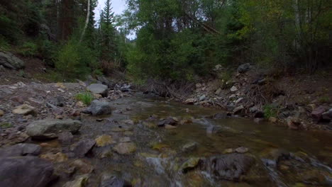 Low-flying-drone-shot-over-a-peaceful-flowing-creek-towards-some-green-trees