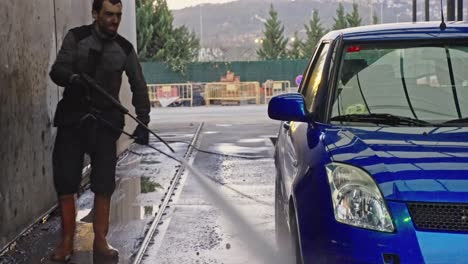 Crouched-man-cleaning-with-a-pressure-water-hose-at-a-car-wash-station