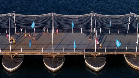 Los-Turistas-Caminan-Por-El-Puente-Pontón-Reina-Emma-Con-Banderas-Festivas-Y-Barandillas.