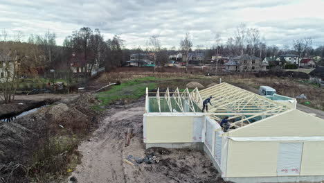 Luftdrohne-über-Haus,-Arbeiter-Bauen-Ein-Dach-Mit-Holzbalken,-Stadtrand