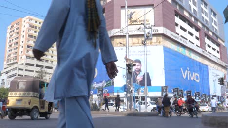 Toma-En-Cámara-Lenta-De-ángulo-Bajo-De-Un-Edificio-Al-Lado-De-Una-Concurrida-Calle-Saddar-Bazar-En-Una-Tarde-Soleada-En-Karachi,-Pakistán