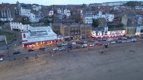 Toma-Panorámica-Aérea-De-Drones-Sobre-La-Playa-En-La-Ciudad-De-Scarborough-En-North-Yorkshire,-Inglaterra,-Reino-Unido,-Durante-La-Noche