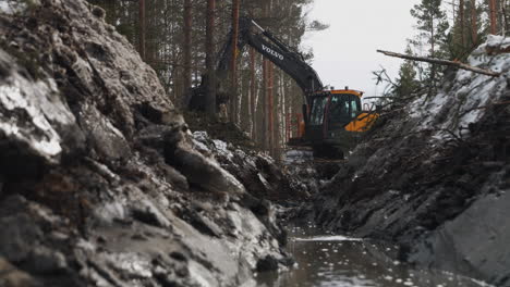 El-Trabajador-De-La-Construcción-Utiliza-Una-Excavadora-Para-Mover-Tierra,-Limpiando-Terrenos-En-El-Bosque-Cerca-Del-Agua.