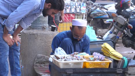 Nahaufnahme-Eines-Ladenbesitzers,-Der-Tagsüber-In-Einem-Schusterladen-Am-Straßenrand-In-Der-Saddar-Bazar-Street-In-Karatschi,-Pakistan,-Mit-Seinem-Kunden-Umgeht