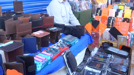 Primer-Plano-Hacia-Atrás-De-Un-Comerciante-Vendiendo-Carteras-Y-Gafas-Templadas-Móviles-En-Un-Puesto-Al-Borde-De-La-Carretera-En-La-Calle-Saddar-Bazar-De-Karachi-Durante-El-Día-En-Pakistán