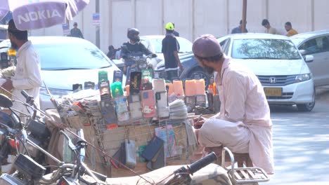 Side-view-shot-of-a-man-checking-records-of-the-sale-of-his-mobile-tempered-glasses-by-his-roadside-shop-at-afternoon-in-Saddar-bazar-Street-in-Karachi,-Pakistan