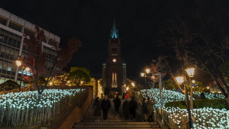 Multitud-De-Personas-Subiendo-Y-Bajando-Las-Escaleras-Frente-A-La-Catedral-De-Myeongdong-Por-La-Noche,-Lapso-De-Tiempo-En-Seúl,-Corea-Del-Sur