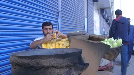 Toma-En-Cámara-Lenta-De-Un-Hombre-Trabajador-Quitando-Semillas-De-Maíz-De-Su-Cuerpo-Para-Venderlas-Durante-El-Día-En-La-Calle-Saddar-Bazar-En-Karachi,-Pakistán