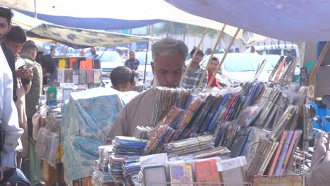 Slow-motion-shot-of-a-shopkeeper-dusting-his-shop-of-mobile-covers-at-a-roadside-stall-in-Saddar-Bazar-Street-during-sunny-afternoon-in-Karachi,-Pakistan