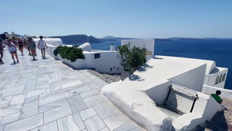 Elders-On-Sidewalk-Near-Store-|-Oia-Santorini-Greece-Greek-Island-in-Aegean-Sea,-Travel-Tourist-Vacation-Immersive-Moving-Walk-Along-Crowds-Shopping-in-White-Marble-Cliffside-and-City,-Europe,-4K