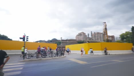 Rome-Immersive-POV:-Moving-In-Busy-Streets-to-Chiesa-Santi-Luca-e-Martina,-Italy,-Europe,-Walking,-Shaky,-4K-|-Large-Crowd-At-Intersection-Gathered-Near-Pole-On-Road-By-Colosseum