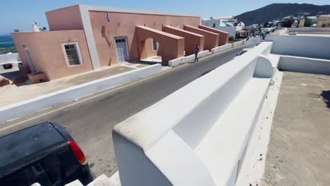 Overlooking-Cars-On-Street-|-Oia-Santorini-Greece-Greek-Island-in-Aegean-Sea,-Travel-Tourist-Vacation-Immersive-Moving-Walk-Along-Crowds-Shopping-in-White-Marble-Cliffside-and-City,-Europe,-4K