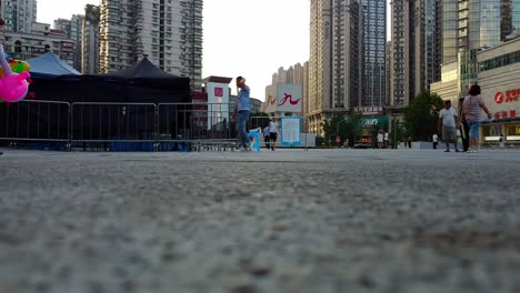 People-walking-with-balloons-at-a-city-square,-buildings-in-the-background-at-dusk-shoot-from-a-low-angle