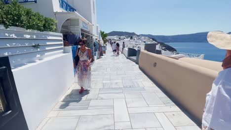 Paar-Geht-In-Der-Nähe-Weiter-Blick-Auf-Das-Meer-|-Oia,-Santorini,-Griechenland,-Griechische-Insel-Im-Ägäischen-Meer,-Reise,-Touristenurlaub,-Immersiver-Wanderspaziergang-Entlang-Der-Menschenmassen,-Die-In-Klippen-Aus-Weißem-Marmor-Und-In-Der-Stadt-Einkaufen,-Europa-4K