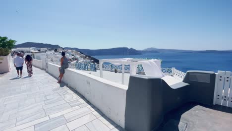 Woman-Staring-At-Marry-Me-Sign-|-Oia-Santorini-Greece-Greek-Island-in-Aegean-Sea,-Travel-Tourist-Vacation-Immersive-Moving-Walk-Along-Crowds-Shopping-in-White-Marble-Cliffside-and-City,-Europe,-4K