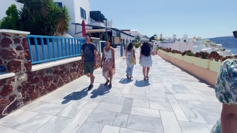 Couple-Walking-On-White-Sidewalk-|-Oia-Santorini-Greece-Greek-Island-in-Aegean-Sea,-Travel-Tourist-Vacation-Immersive-Moving-Walk-Along-Crowds-Shopping-in-White-Marble-Cliffside-and-City,-Europe,-4K