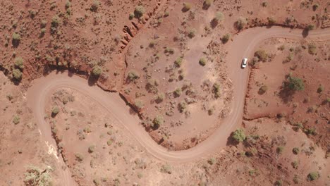 Bird's-eye-view-of-white-car-driving-on-winding-dirt-road-in-Flinders-Ranges,-South-Australia