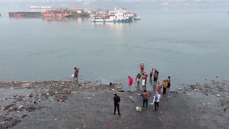 Foto-Superior-De-Unos-Pocos-Hombres-Bañándose-En-La-Orilla-De-Un-Mar-Con-Un-Barco-Al-Fondo-Durante-Una-Mañana-De-Invierno-En-Calcuta,-India.