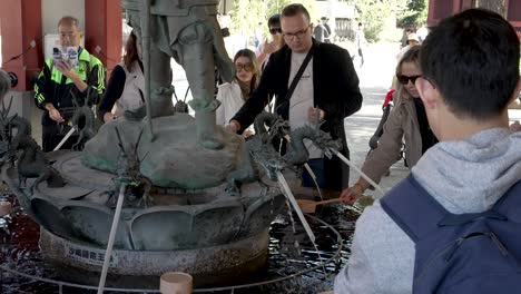 Escena-En-Cámara-Lenta-De-Personas-En-Una-Fuente-De-Purificación-De-Agua-En-El-Templo-Sensoji,-Japón