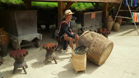 Pueblo-De-Cu-Lan-En-La-Ciudad-De-Da-Lat---Un-Artista-Vietnamita-Toca-Un-Gran-Tambor-étnico-En-La-Calle,-Viejos-Muebles-Retro-En-El-Fondo---Cámara-Lenta